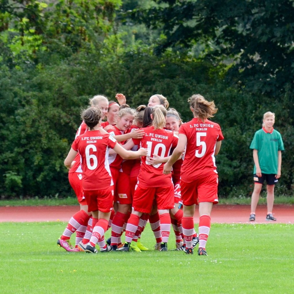Eine Gruppe von Frauen in roten Fußballtrikots feiert einen Torerfolg auf dem Spielfeld.