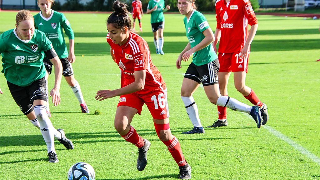A soccer match between two women's teams on a green field, a player with the ball in the center.