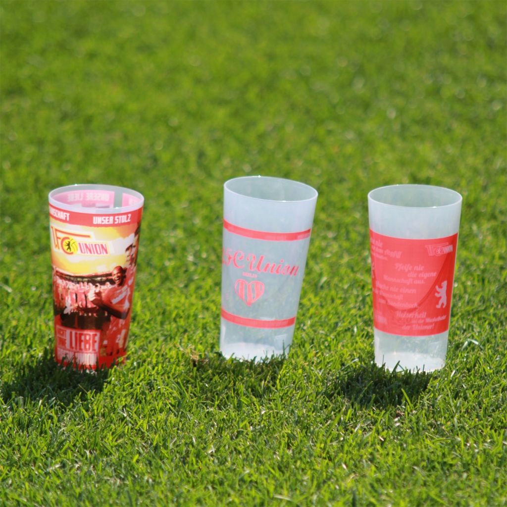 Drei transparente Becher mit verschiedenen Designs auf einer grünen Rasenfläche.