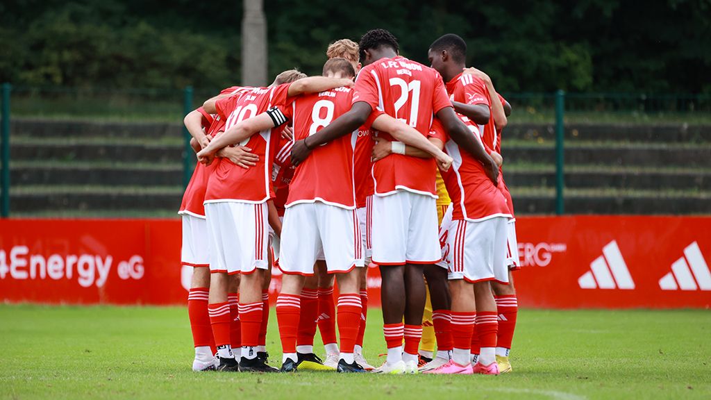 A group of football players in red jerseys is huddled together on a training field.