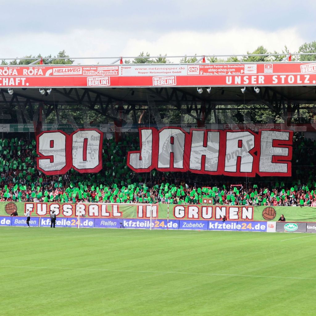 Fanbanner im Stadion mit dem Text "90 Jahre Fußball in Grün" vor einer großen Menge in grüner Kleidung.