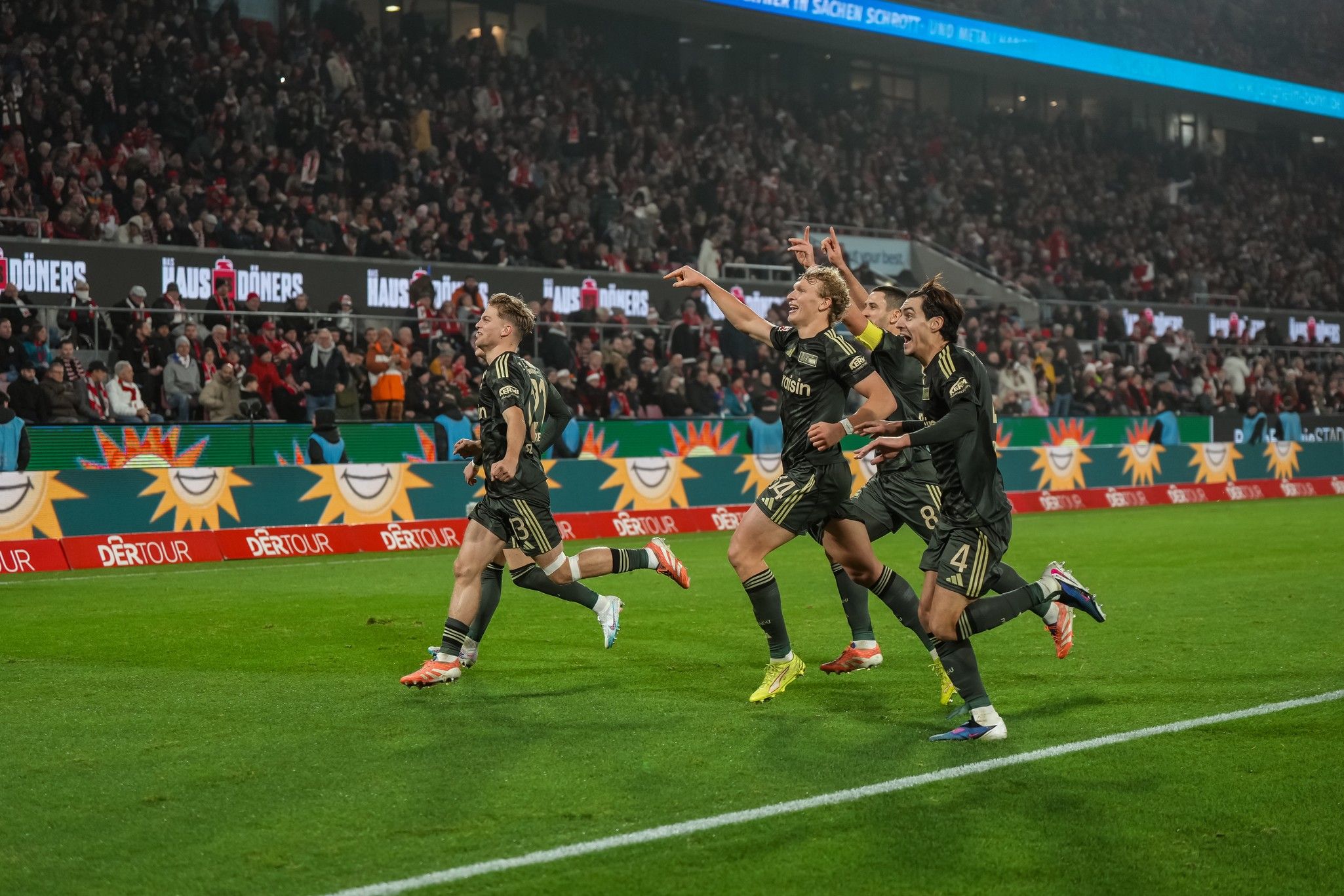 Spieler des FC Bayern München feiern einen Torerfolg auf dem Spielfeld, umgeben von jubelnden Fans.