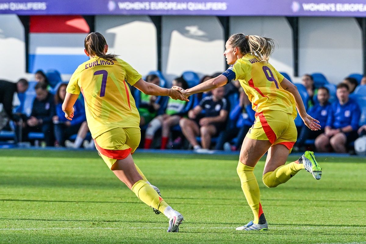 Zwei Spielerinnen in gelben Trikots feiern einen gemeinsamen Moment auf dem Fußballplatz.