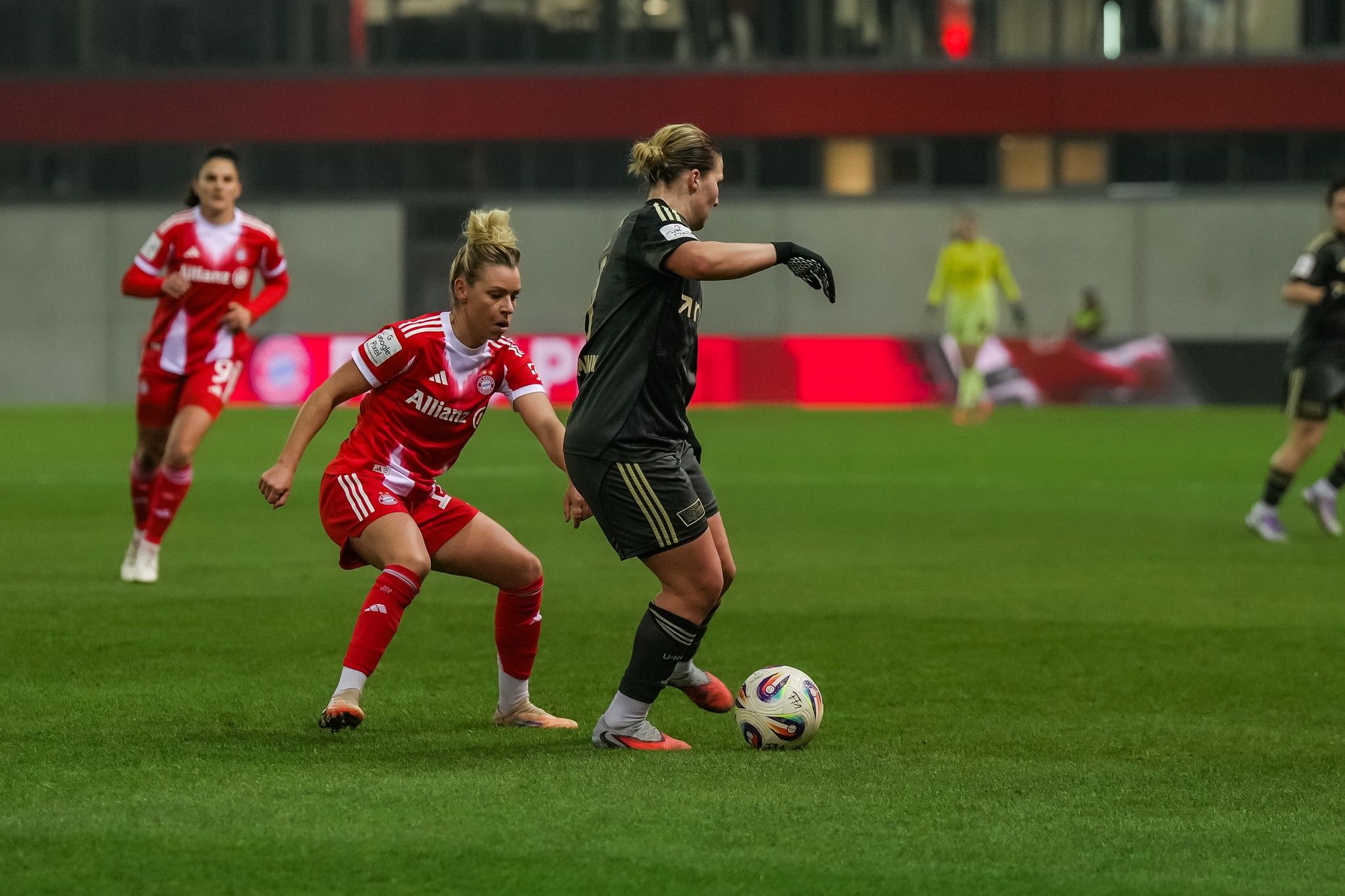 Zwei Fußballspielerinnen im Wettkampf um den Ball auf einem Kunstrasenplatz während eines Spiels.