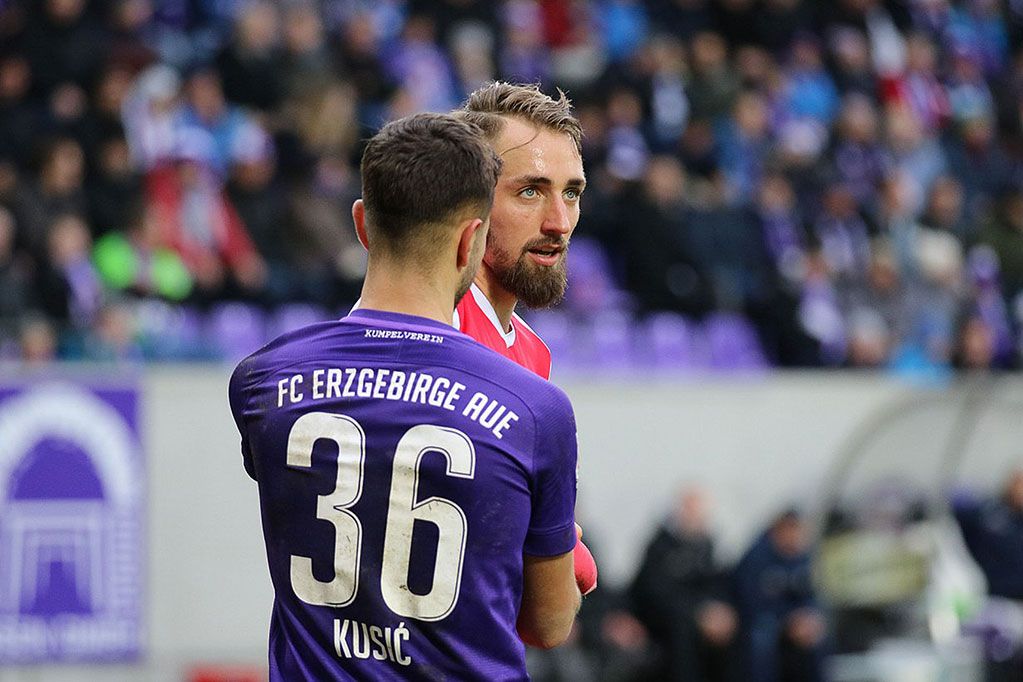 Two soccer players are on the field, one wearing jersey number 36 with the name Kusić, the other in red.