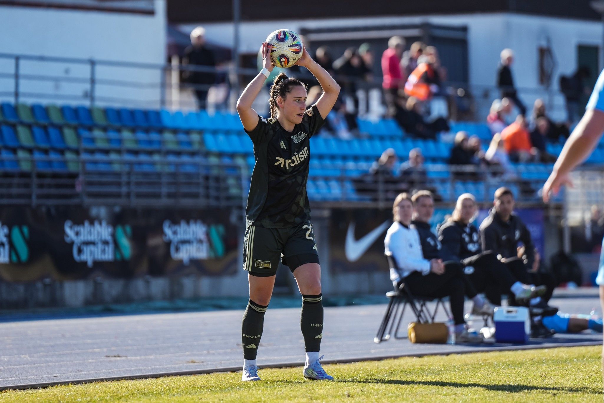 Spielerin führt einen Einwurf im Fußballspiel aus, während das Team auf der Bank zuschaut.