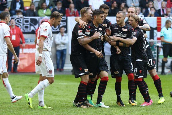 Black soccer players celebrate a goal while some players in white stand in the background. Stadium atmosphere.