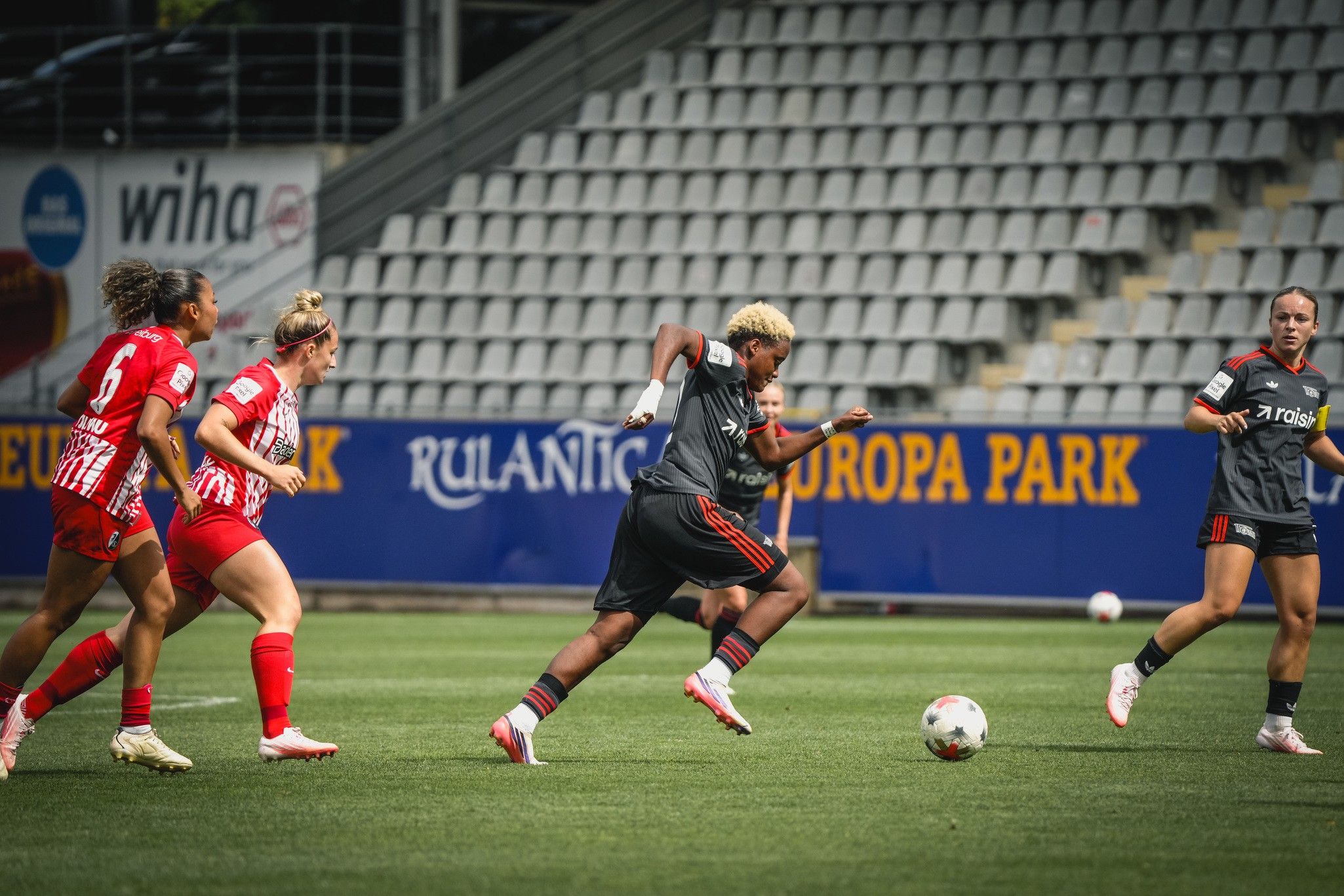 Eine Fußballspielerin sprintet über das Feld, während drei Gegnerinnen ihr folgen. Echter Sport mit intensiver Dynamik.