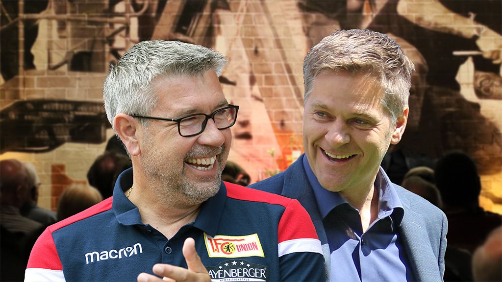 Two smiling men in modern clothing against a blurred background suggesting a gathering.