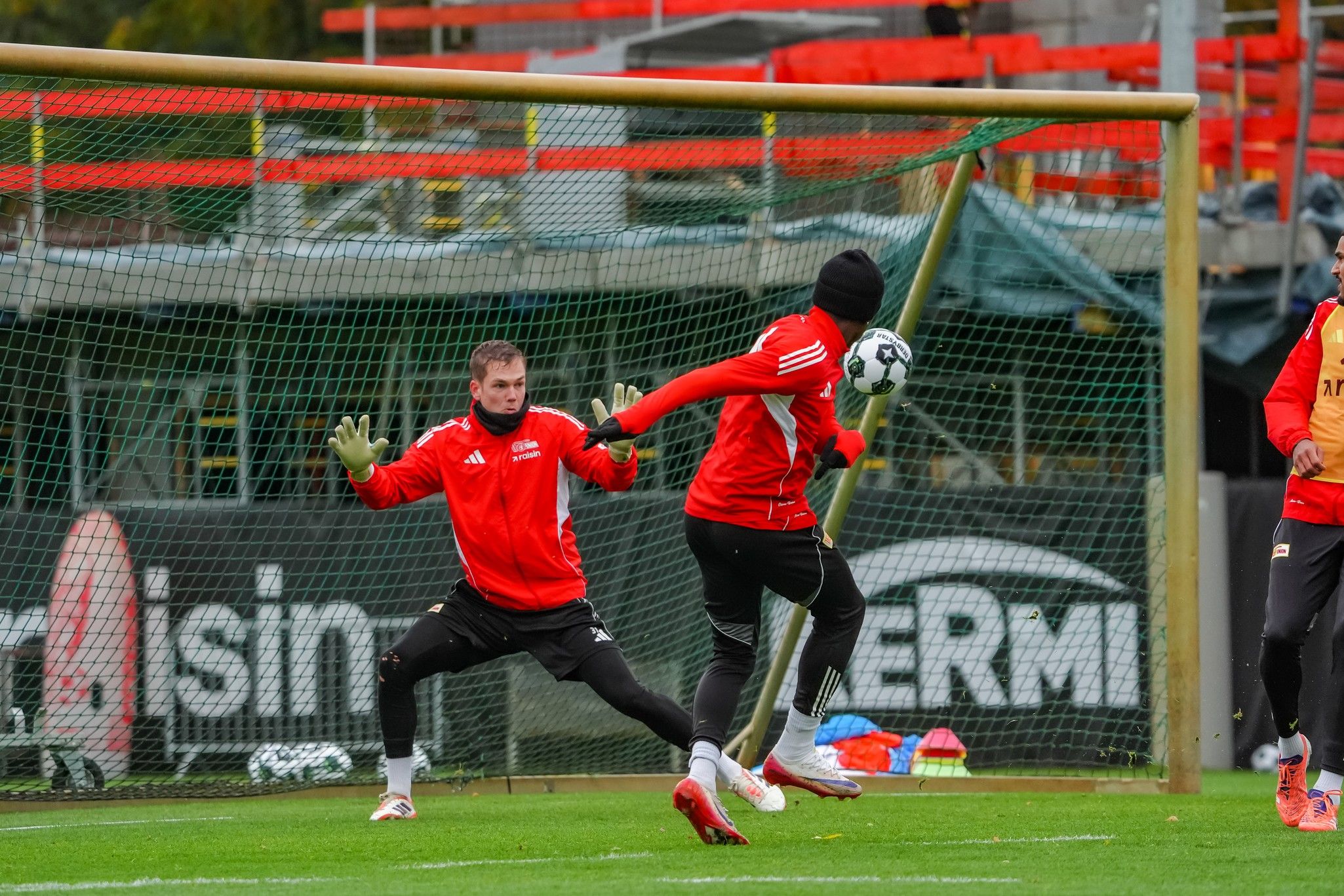 Torwart im Training, während ein Spieler einen Schuss mit einem Fußball abfängt. Im Hintergrund steht ein weiteres Tor.