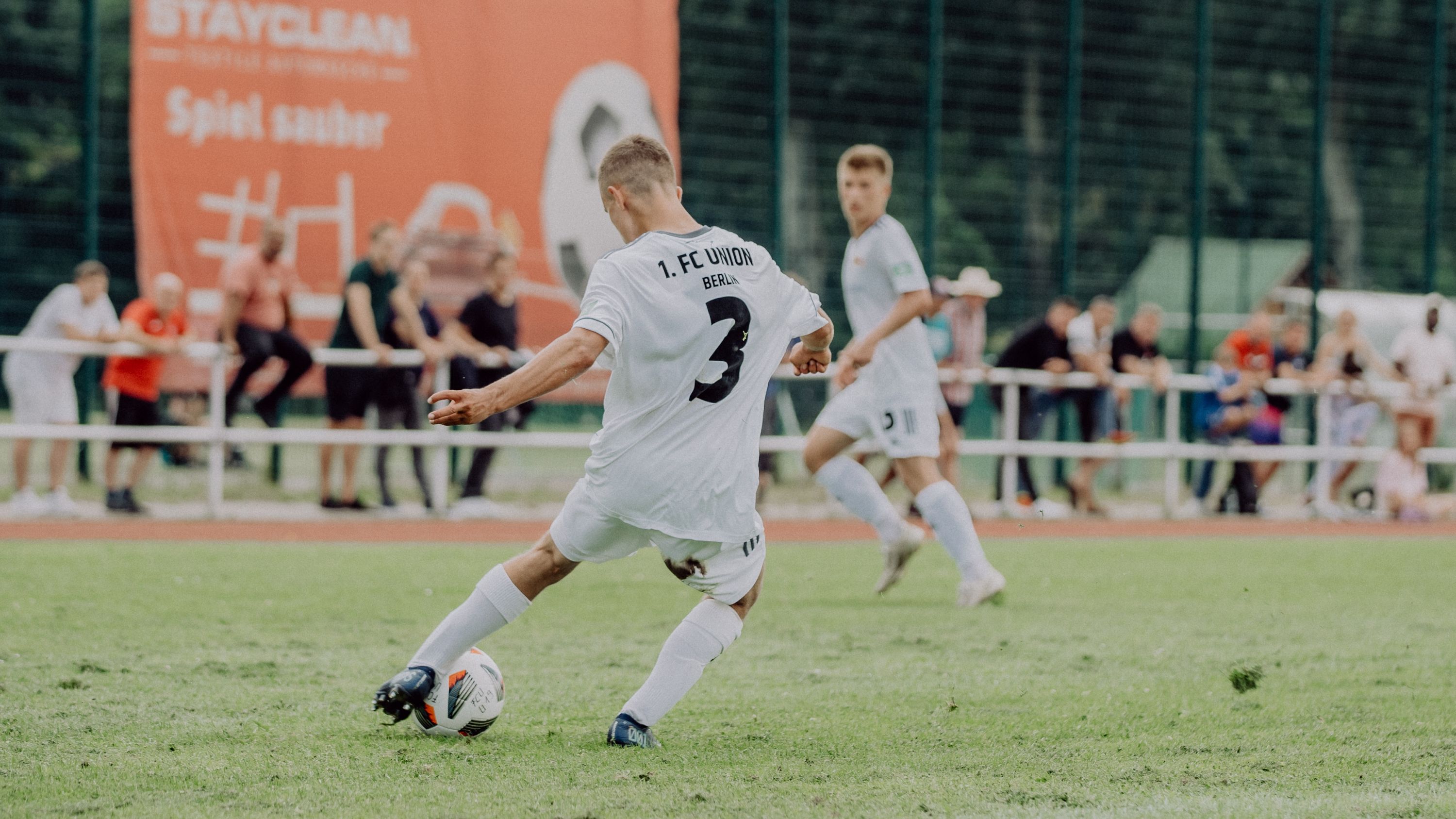 A soccer player in a white jersey with the number 3 is preparing to shoot, while spectators watch in the background.