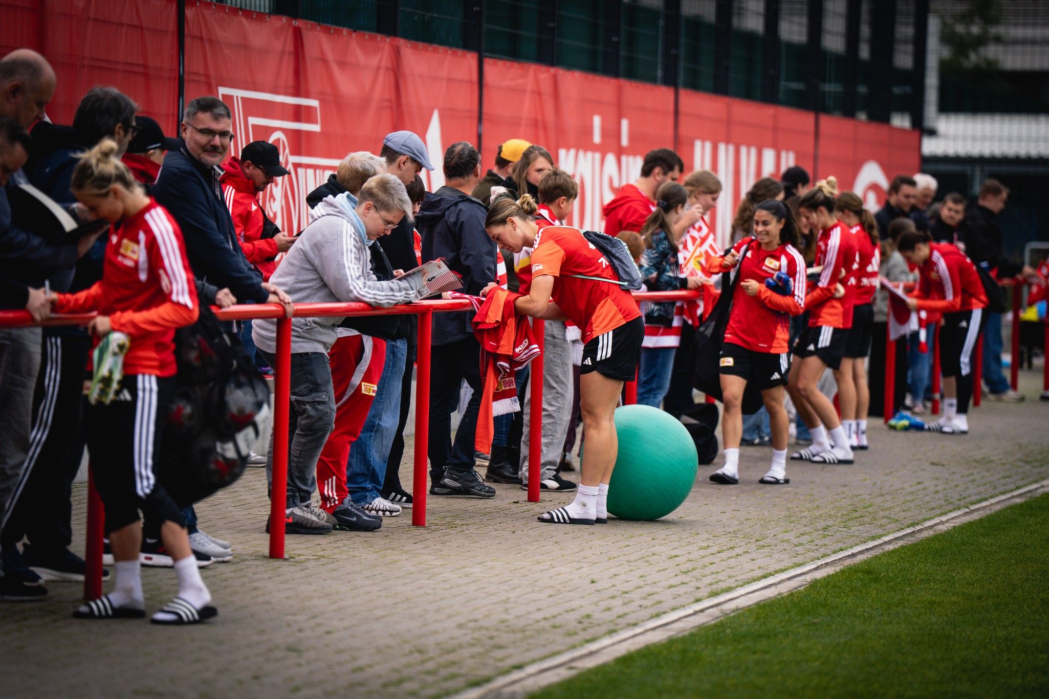 Gruppierung von Fans und Spielerinnen bei einer Sportveranstaltung, die Autogramme sammeln und sich austauschen.