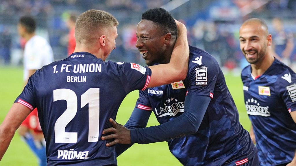 Spieler des 1. FC Union Berlin feiern einen Torerfolg, umarmt in Trikots mit Vereinslogo auf dem Spielfeld.