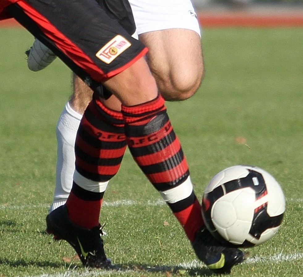 Ein Fußballspieler in gestreiften Socken tritt einen Fußball auf einem grünen Rasenfeld.