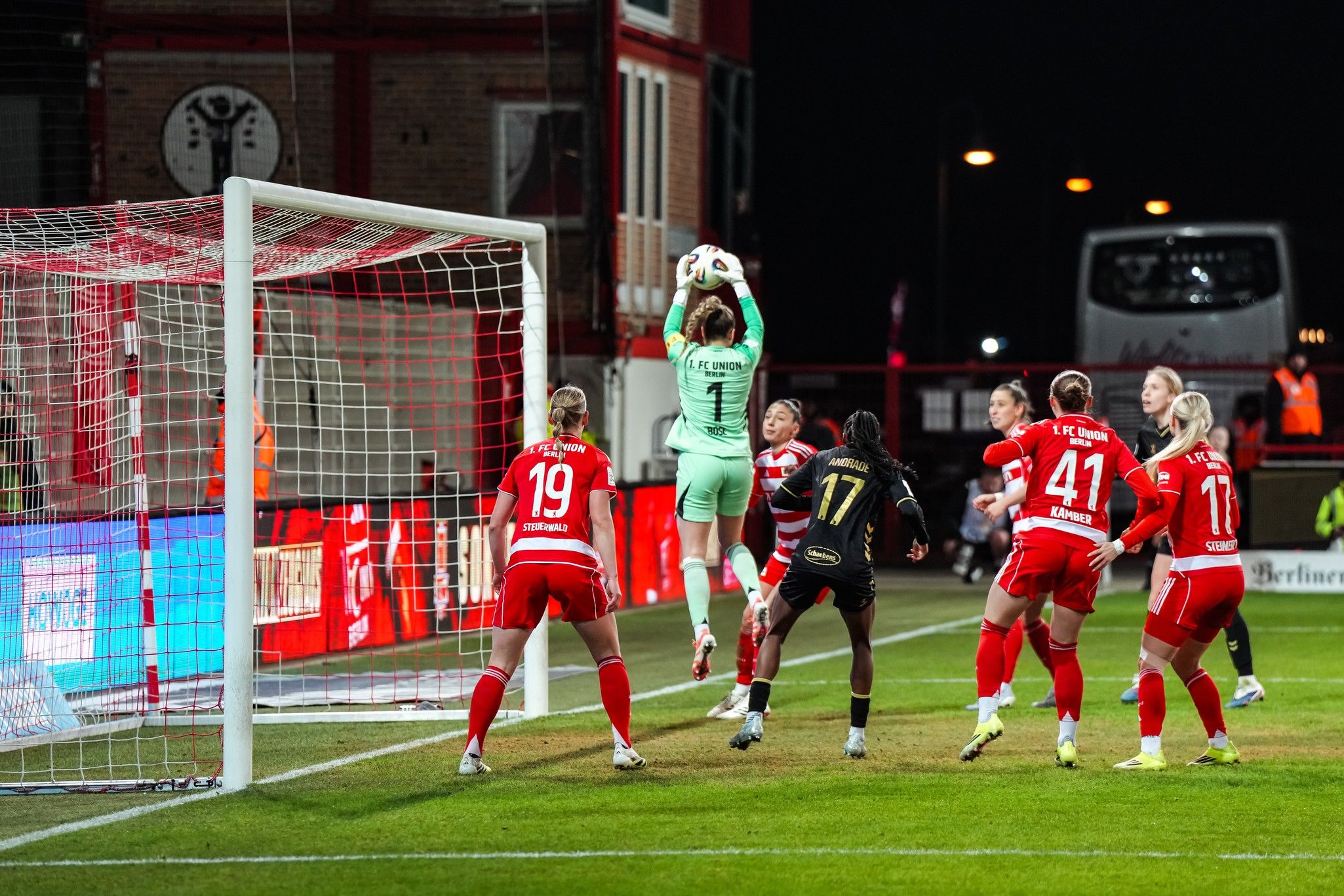 Torhüterin springt hoch, um den Ball zu fangen, während mehrere Spielerinnen des gegnerischen Teams in der Nähe stehen.