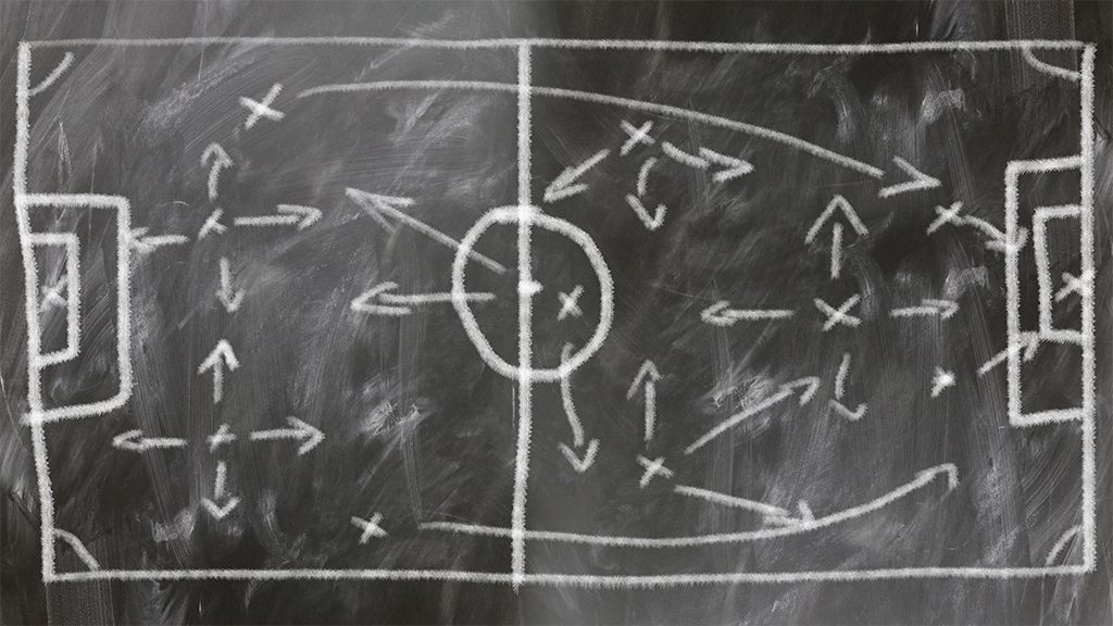 Tafel mit einer Zeichnung eines Fußballfeldes, auf dem Spielzüge und Positionen mit Kreide skizziert sind.