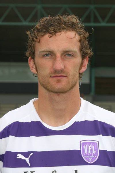 Porträt eines Mannes mit lockigem Haar, der ein gestreiftes Trikot in Lila und Weiß trägt.