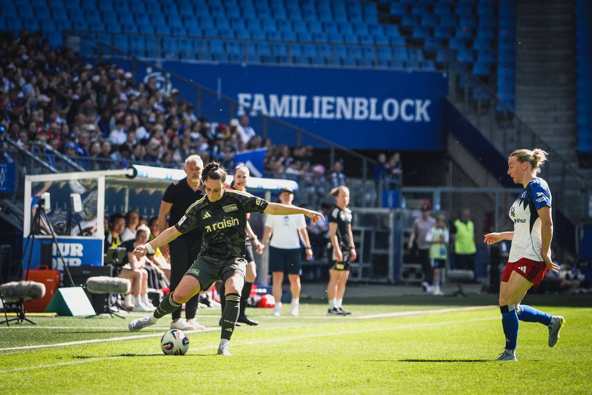 Spielerinnen auf dem Fußballfeld während eines Spiels. Eine Spielerin führt einen Einwurf aus, Zuschauer im Hintergrund.