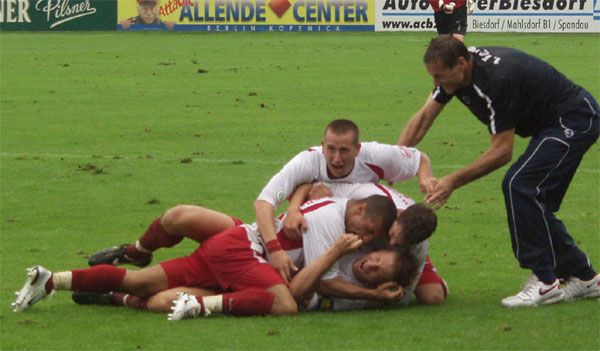 Eine Gruppe von Fußballspielern feiert einen Treffer, indem sie sich jubelnd auf dem Rasen zusammenrotten.