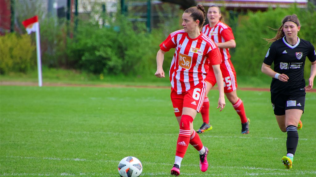 Zwei Fußballspielerinnen auf dem Spielfeld, eine in rot-weiß gestreiftem Trikot, die andere in schwarzem Trikot.