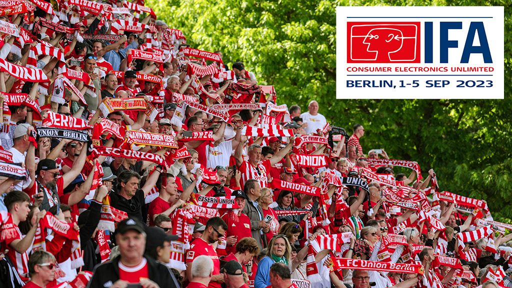 Eine große Menschenmenge in Fußballtrikots schwenkt Schals in den Farben Rot und Weiß, mit einem Logo der IFA 2023 im Hintergrund.
