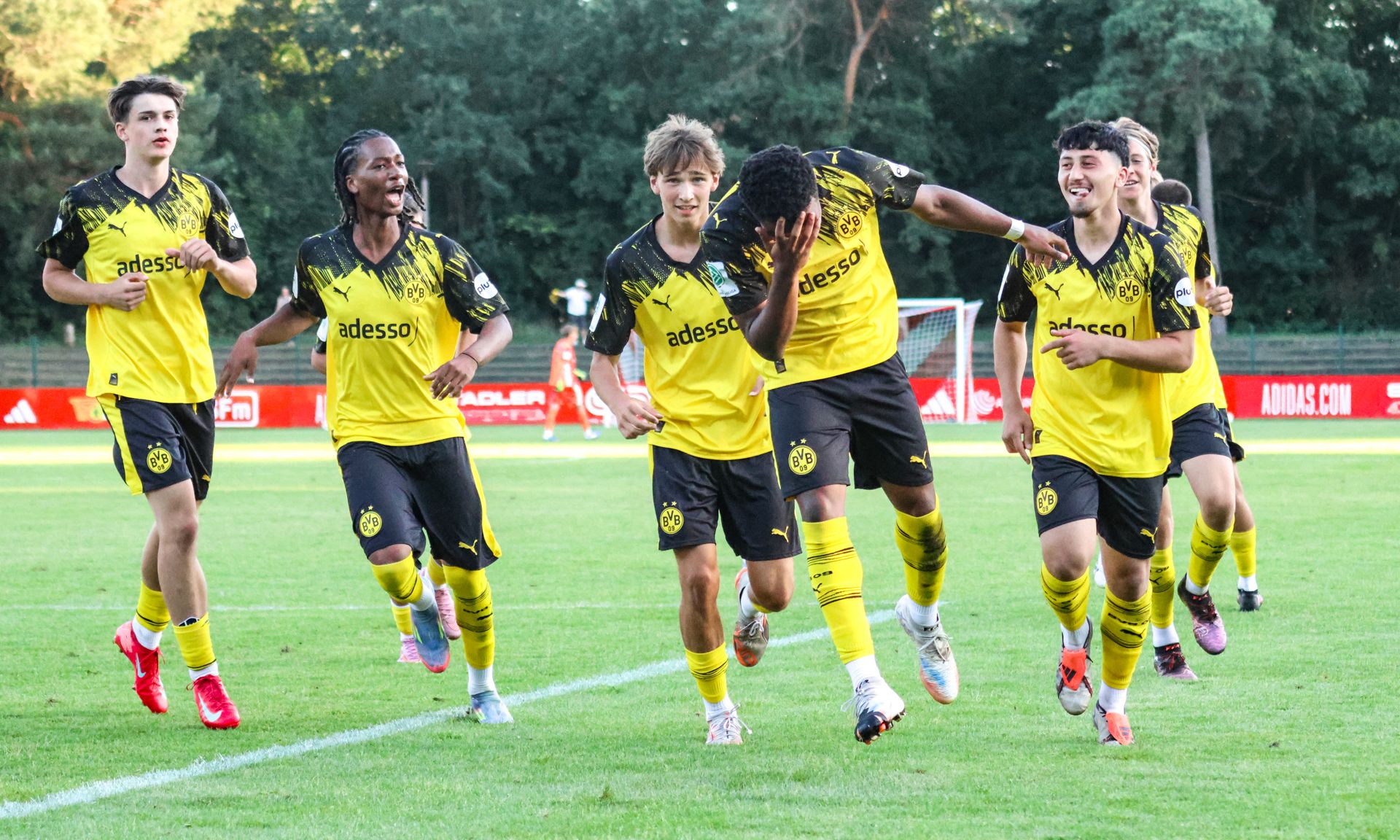 Jugendfußballmannschaft in gelb-schwarzen Trikots jubelt nach einem Tor auf dem Platz.