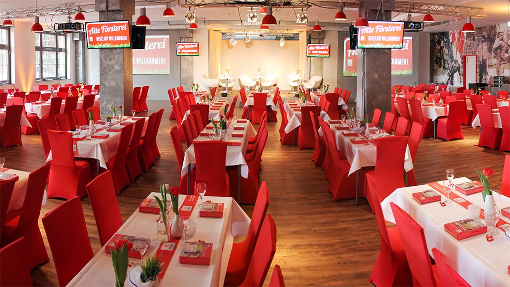 Ein großzügig gestellter Restaurantbereich mit roten Stühlen, weißen Tischen und Blumendekoration, bereit für eine Veranstaltung.