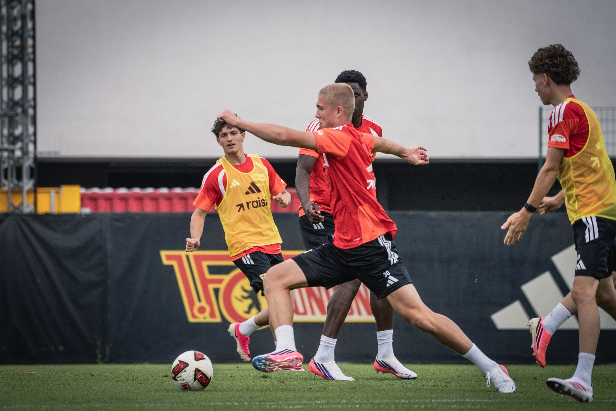 Gruppentraining einer Fußballmannschaft auf dem Feld, Spieler in roten Trikots und Trainingswesten, Ball wird geschossen.