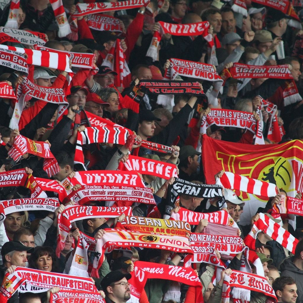 Eine Menschenmenge in einem Stadion hält zahlreiche Schals mit dem Schriftzug "EISERN UNION" hoch.