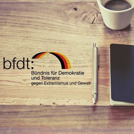 Logo des Bündnisses für Demokratie und Toleranz mit einem Kaffeebecher und einem Notizbuch auf einem Tisch.