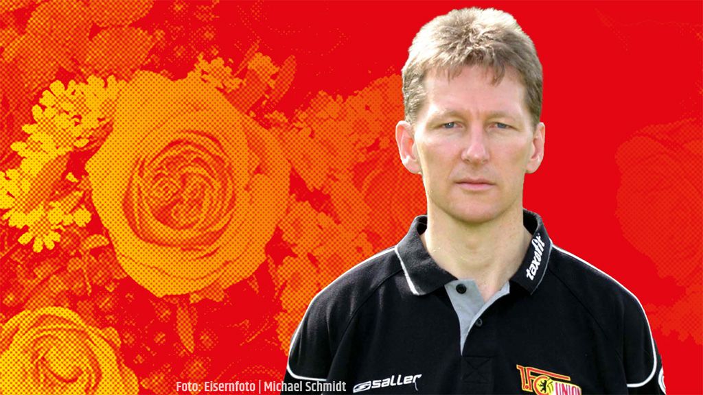 Ein Mann mit kurzem Haar und einem schwarzen Polohemd steht vor einem farbigen Hintergrund mit Rosenmustern.