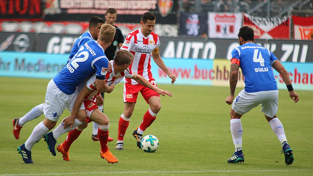 Fußballspiel mit Spielern in blauen und roten Trikots während eines Spiels auf einem Stadionfeld.