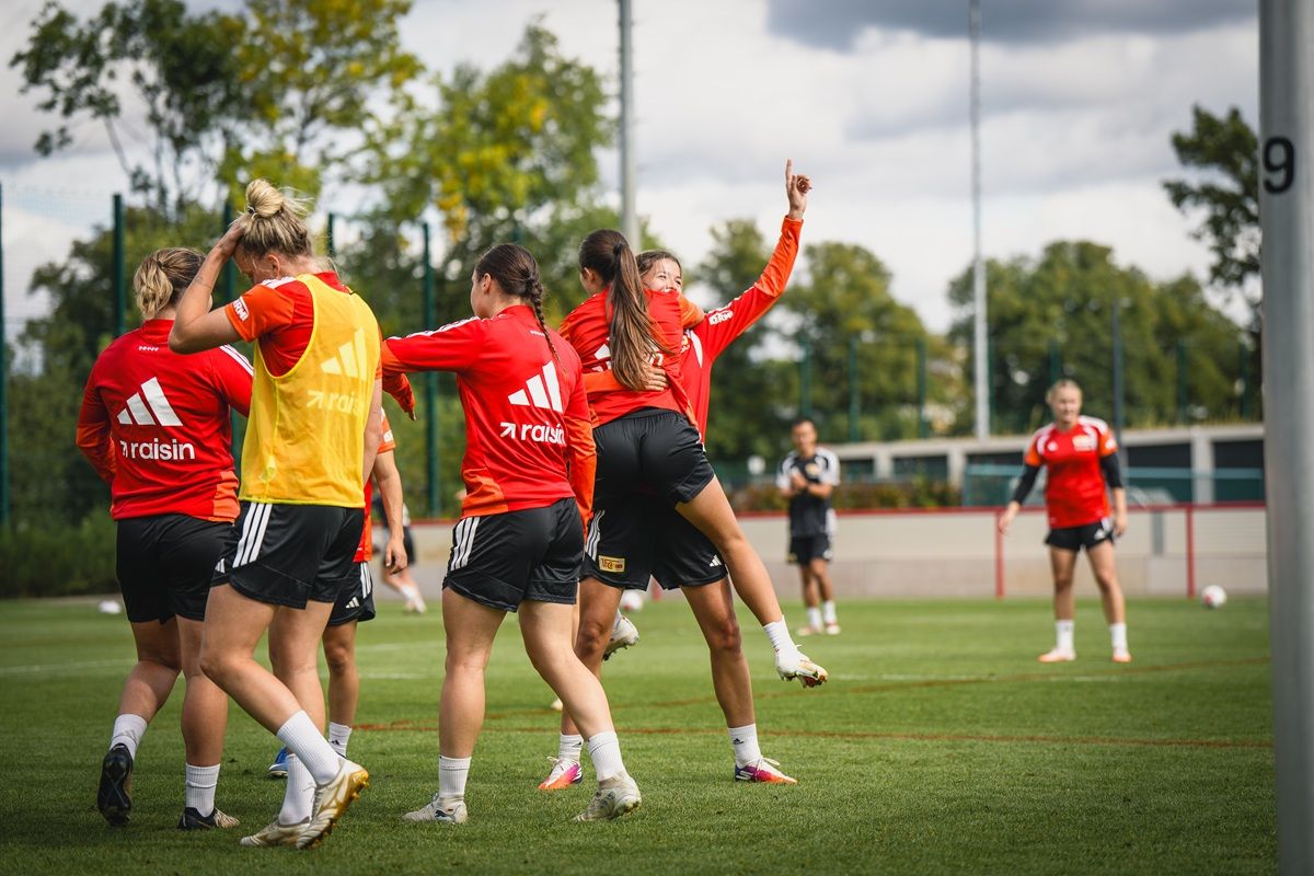 Eine Gruppe von Fußballspielerinnen in rot-weißen Trikots trainiert auf einem grünen Spielfeld.