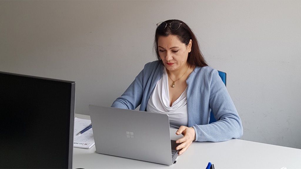 Eine Frau sitzt an einem Schreibtisch und arbeitet konzentriert an einem Laptop.