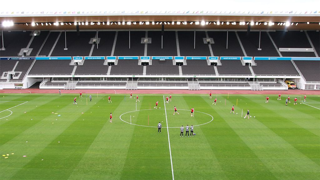 Eine weitläufige Sportarena mit Spielern, die auf dem Rasen trainieren, und Trainern, die Anweisungen geben.