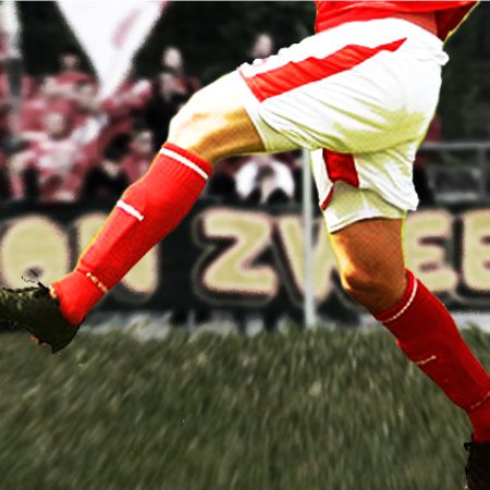 Ein Fußballspieler in rot-weißer Uniform schießt den Ball auf einem grünen Feld.