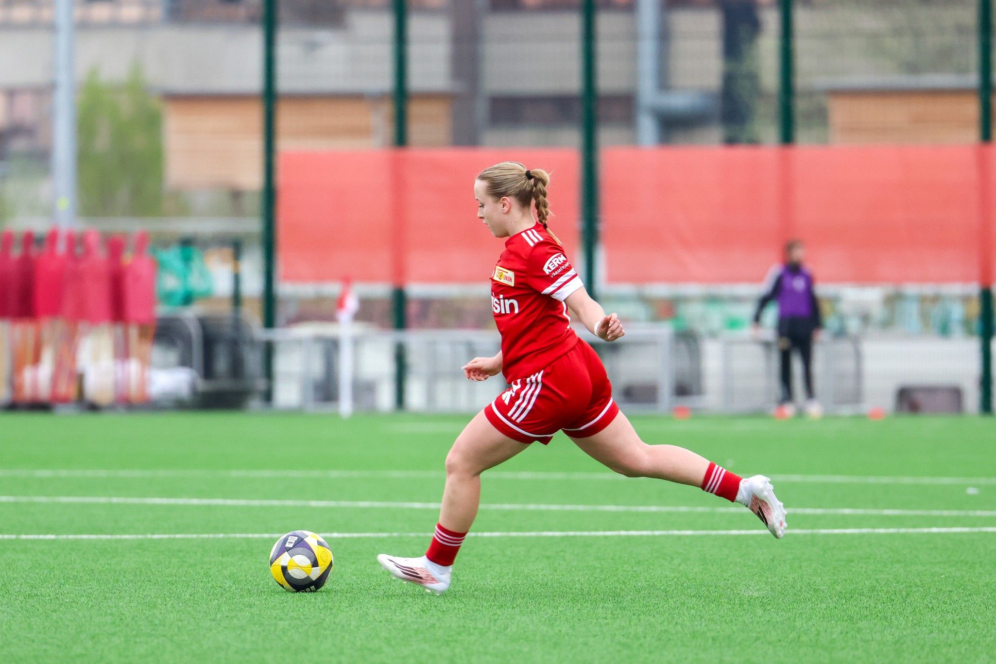 Eine Spielerin in rotem Trikot läuft über ein Fußballfeld, um den Ball zu spielen.