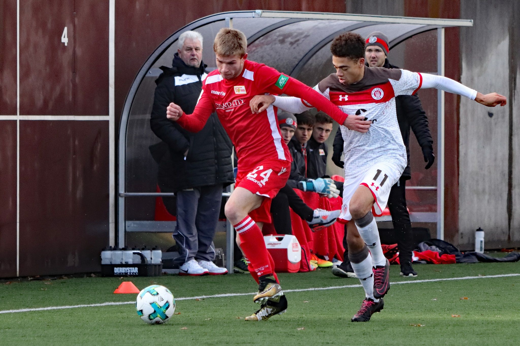 Two soccer players are battling for the ball in a competition, while spectators watch from the sidelines.