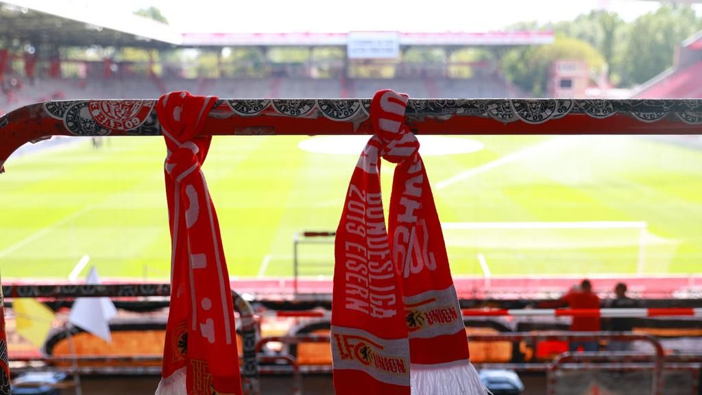 Rote Fanschals hängen an einem Stadionbalken, im Hintergrund ist das Spielfeld und die Tribünen sichtbar.