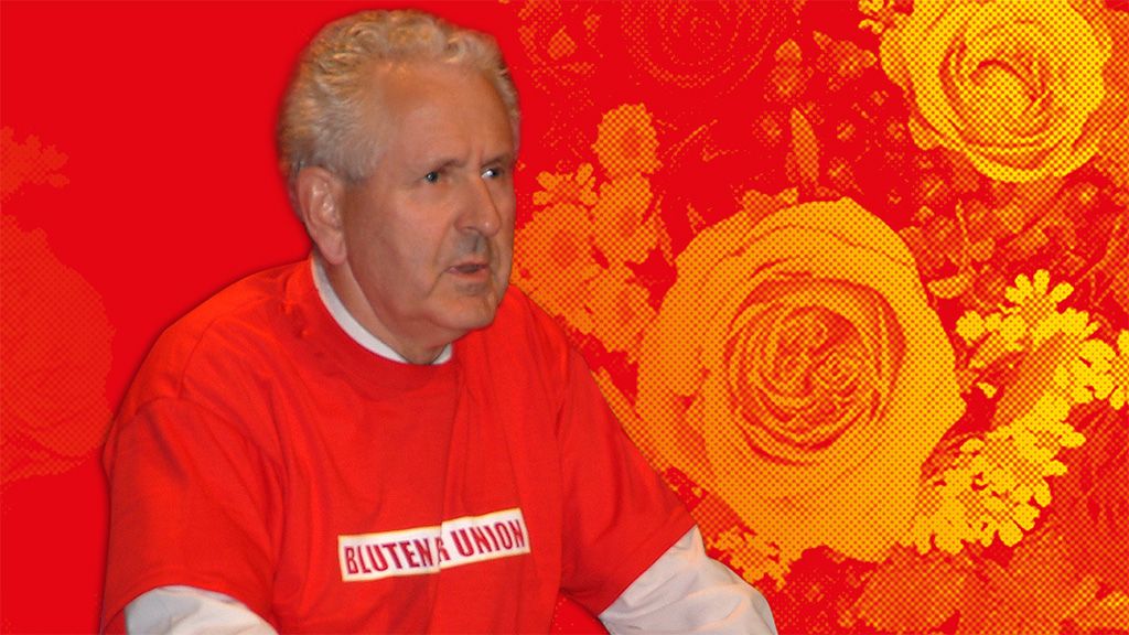Ein älterer Mann in einem rotem T-Shirt mit der Aufschrift „BLUTEN UNION“, vor einem roten Hintergrund mit Blumenmotiven.