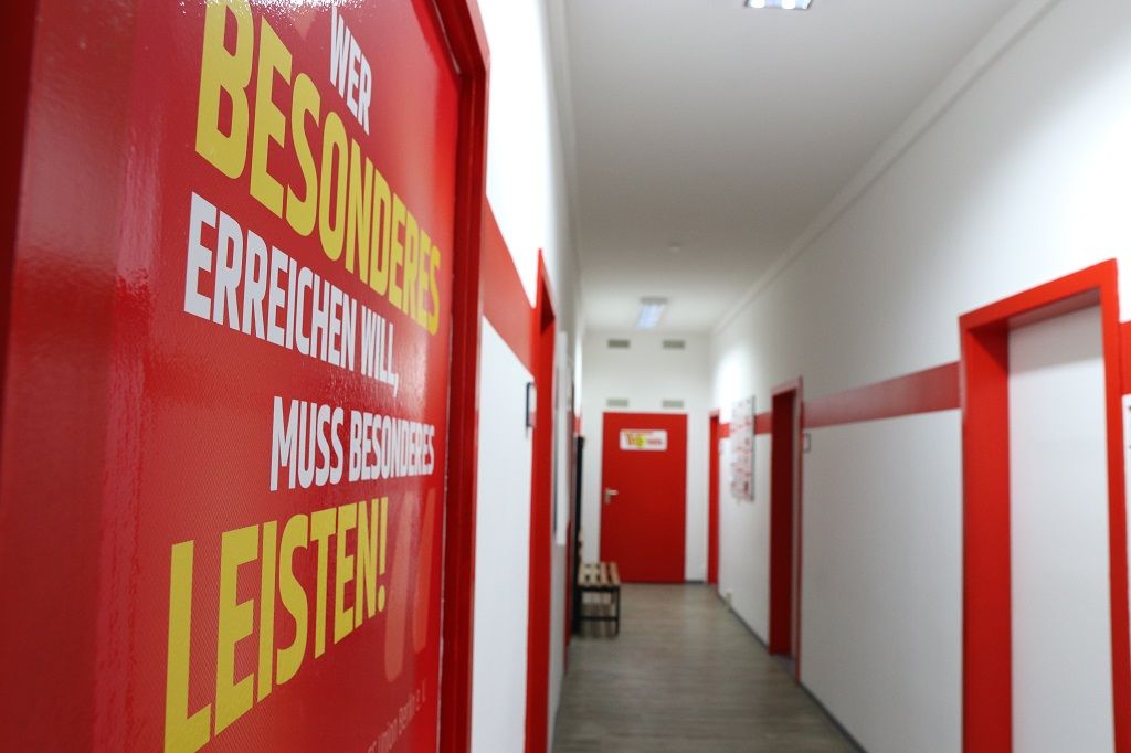 Ein langer Flur mit roten Türen und Wänden, an denen auffällige gelbe Sprüche stehen.