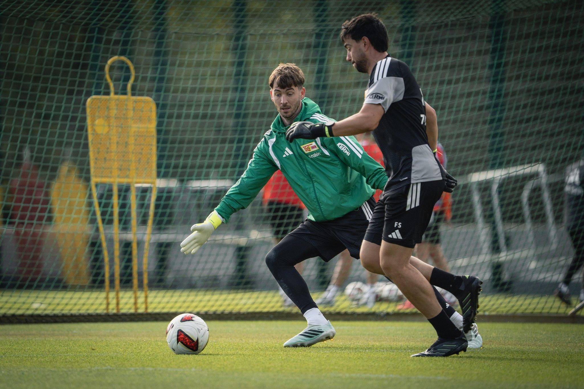 Ein Torwart in grüner Ausrüstung versucht, einen Ball während des Trainings von einem angreifenden Spieler abzuwehren.