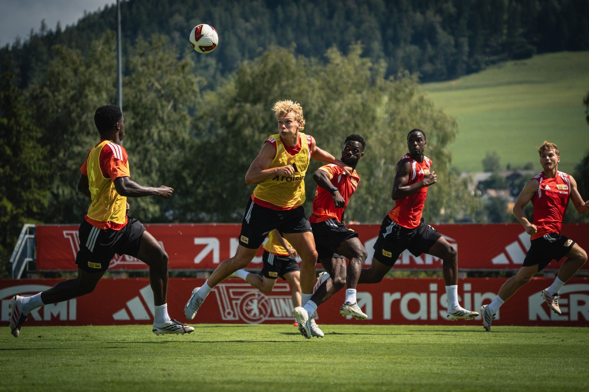 Fußballspieler trainieren auf einem Platz, während ein Spieler den Ball in Richtung seines Mitspielers passt.
