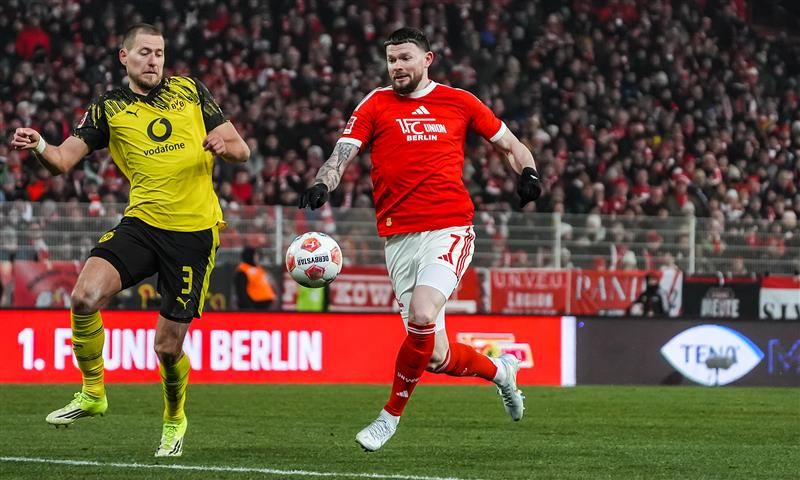 Ein Spieler in roter Kleidung dribbelt den Ball, während ein Verteidiger in gelber Kleidung ihn zu stoppen versucht.