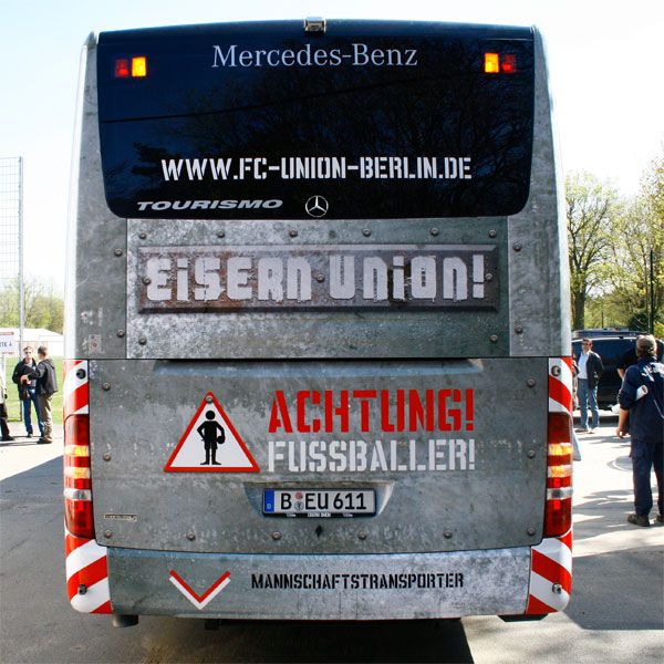 Bus der Mannschaft "Eisern Union" mit auffälligem Design und Warnhinweis für Fußballer.