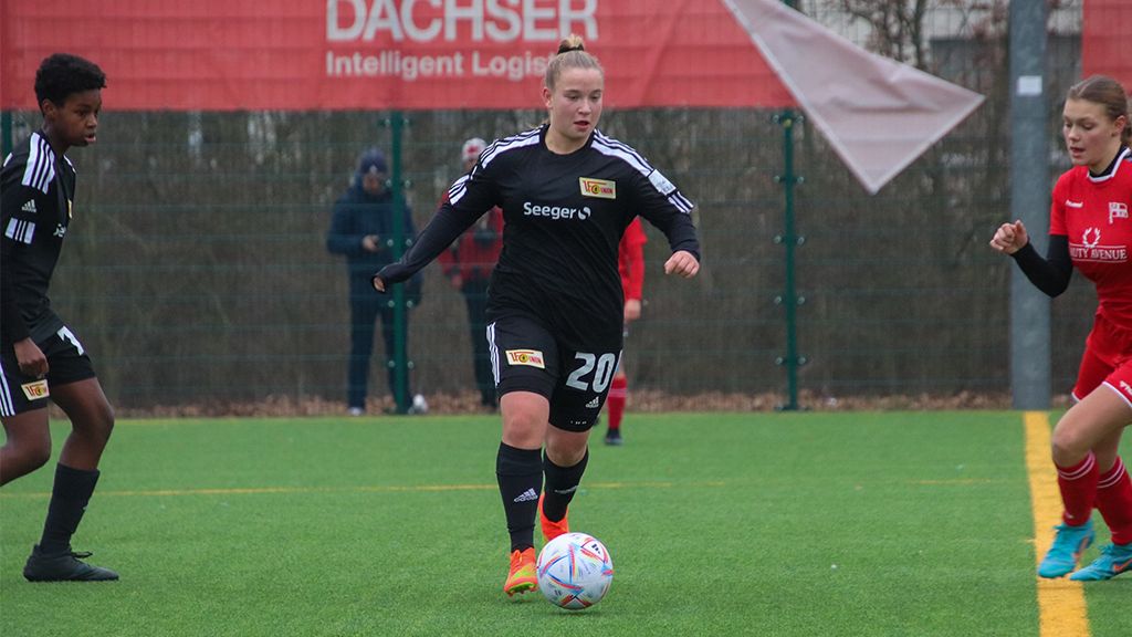 Junge Fußballspielerin in schwarzem Trikot dribbelt den Ball auf einem Kunstrasenplatz, umgeben von anderen Spielern.
