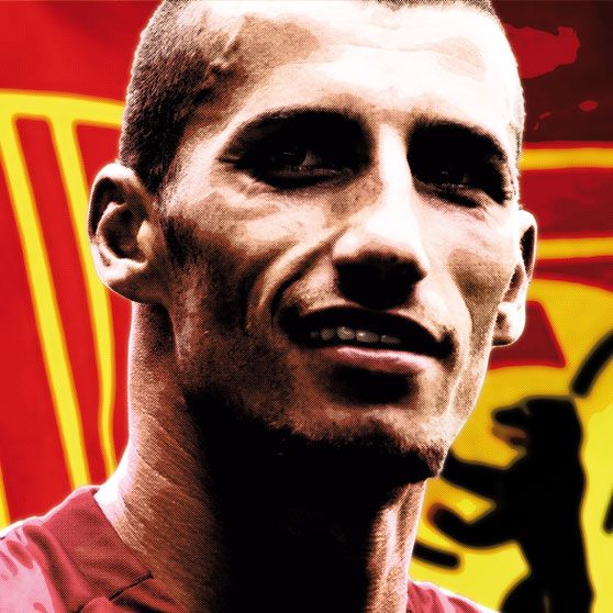 Porträt eines Fußballspielers vor einem Hintergrund mit einem roten und gelben Muster und einem Wappen.