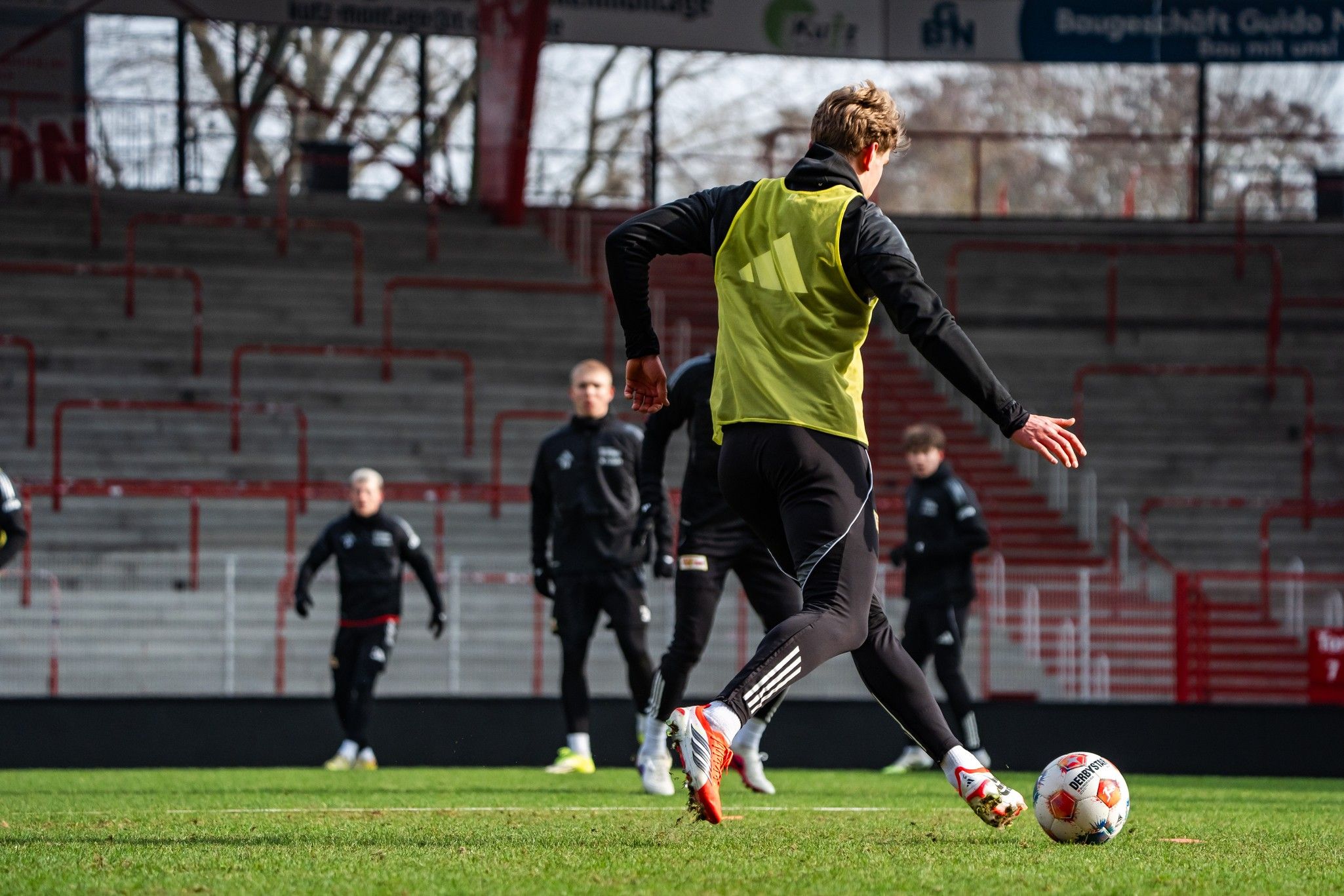 Fußballspieler in Trainingskleidung führt einen Schuss auf ein Tor aus, während andere Spieler im Hintergrund trainieren.