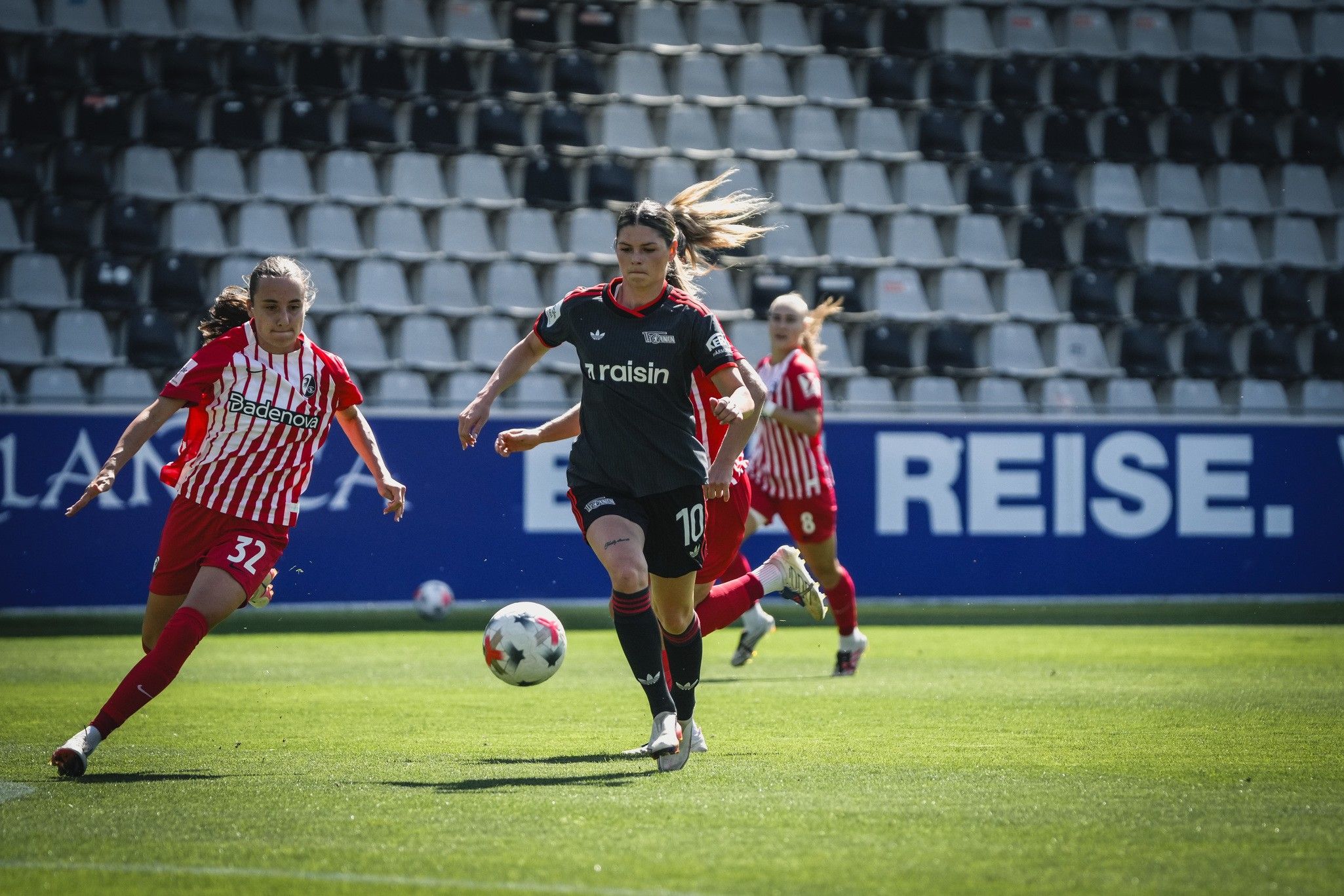 Eine Fußballspielerin in schwarzer Uniform mit der Nummer 10 dribbelt den Ball, während eine Gegnerin in rot-weißer Uniform hinter ihr folgt.