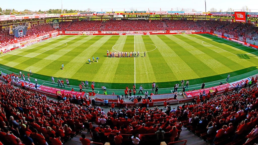 Overview of a packed football stadium with spectators in red T-shirts and players on the field.